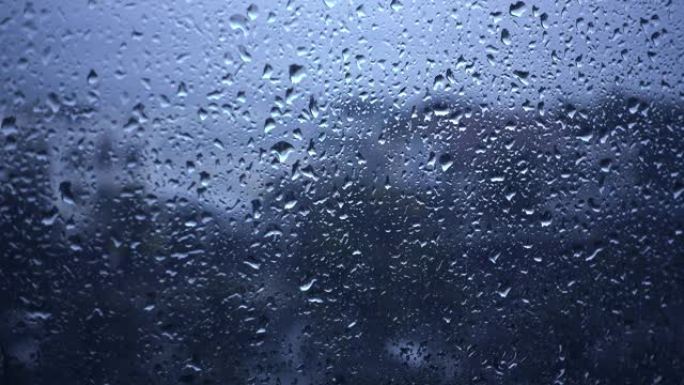 雨滴落在窗户上的特写镜头，望着多云的阴天