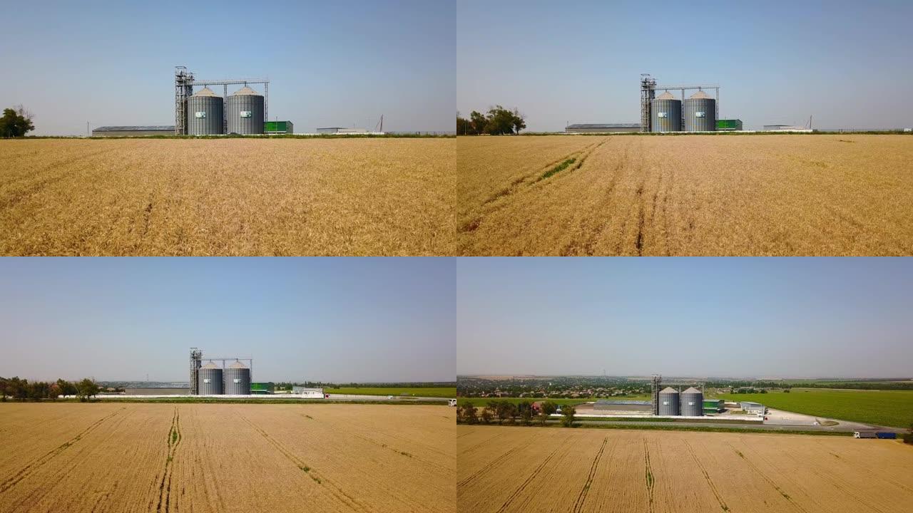 麦田前的谷物升降机天线。四轴飞行器无人机摄像机从面粉或油厂飞来。农田附近的筒仓。农业主题，收获季节。