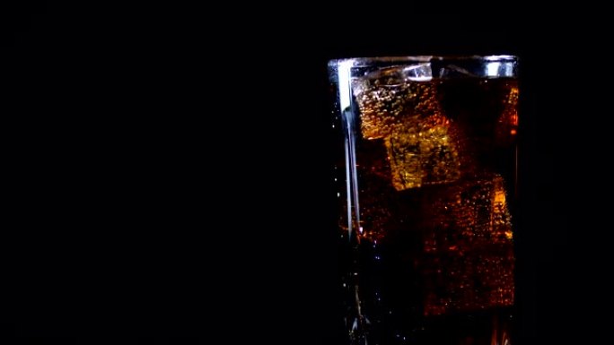 可乐配冰块。旋转玻璃的侧视图，其中冷碳酸棕色甜饮料倒在黑色背景上，与自由复制空间隔离。慢动作200 