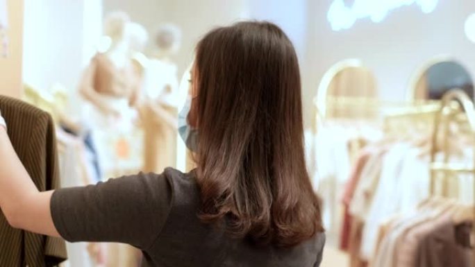 亚洲woung女人购物狂在商店和时尚精品店的衣架上看起来时髦的红色连衣裙，特写镜头，她戴着保护面具在