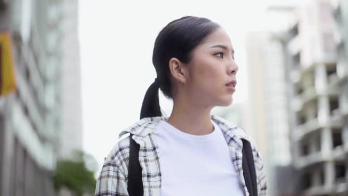 年轻的亚洲女性背包客穿着aloha衬衫在城市旅行，她站在城里，环顾四周时感到怀疑。慢动作镜头。