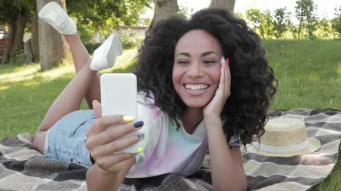 积极的非洲裔美国女孩在公园的格子上用智能手机自拍