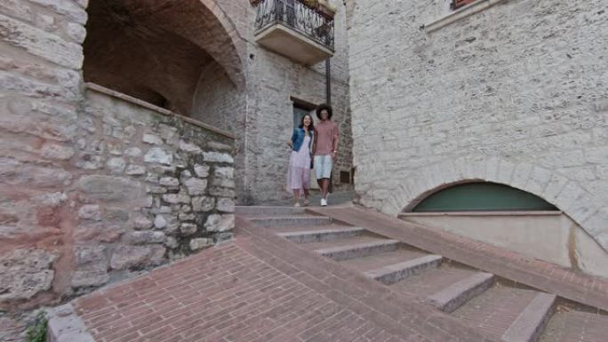 浪漫的夫妇步行参观阿西西的乡村小镇。侧面跟随。翁布里亚的朋友意大利之旅。4k慢动作