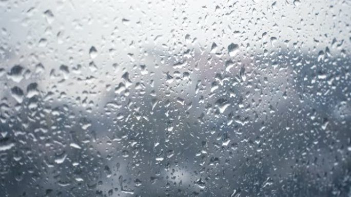 雨滴落在窗户上的特写镜头，望着多云的阴天