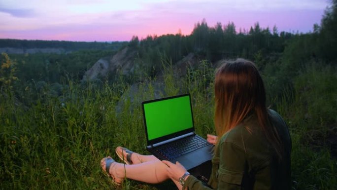 年轻女孩在山顶上绿屏的笔记本电脑上工作。