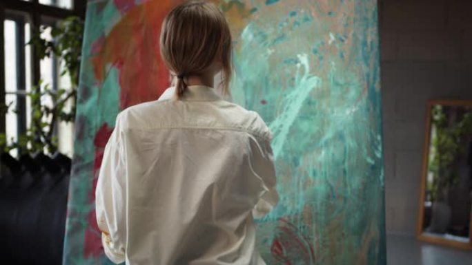 女艺术家走近这幅画，从画笔上喷洒颜料。