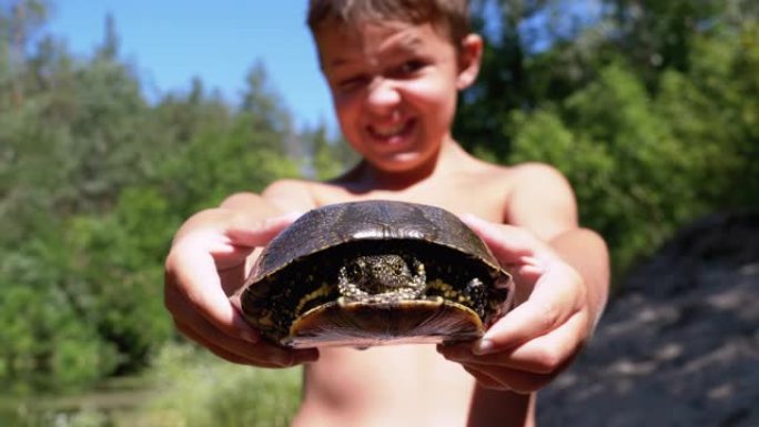 男孩抱着乌龟，在绿色植被的河上恶毒地微笑