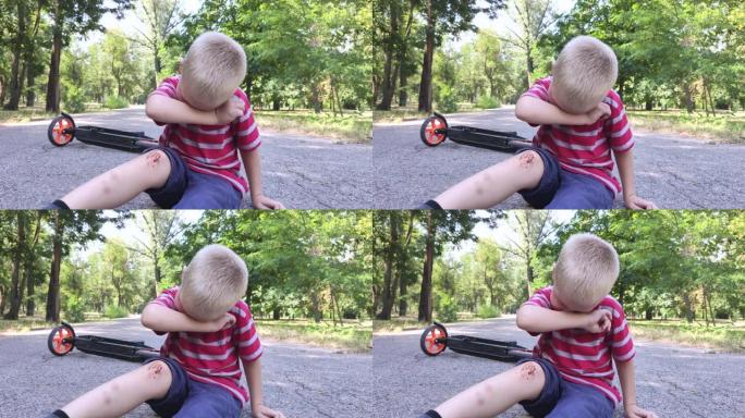 一个四岁的孩子从踏板车上摔下来，膝盖受伤。孩子哭了，擦着膝盖，在上面吹。草率驾驶和父母粗心的概念。