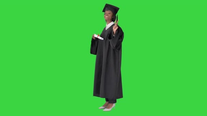 微笑的非裔美国女学生穿着毕业长袍，在绿屏上与文凭合影，色键