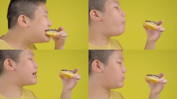 肥胖的亚洲青春期男孩吃黄色背景的甜甜圈。