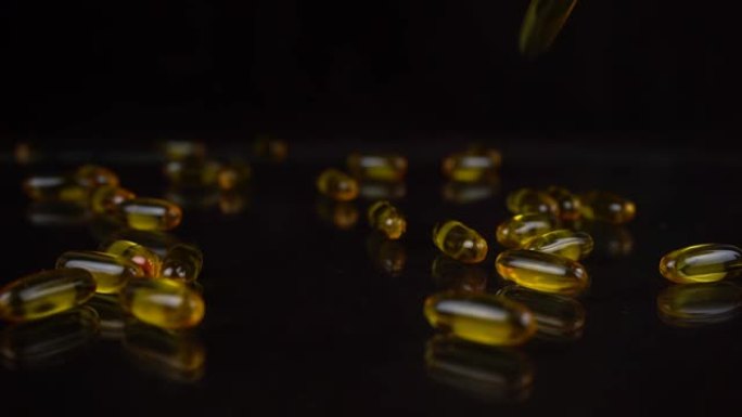 黑色镜子背景下落下的欧米茄3鱼油胶囊的慢动作拍摄。凝胶壳中的金色维生素