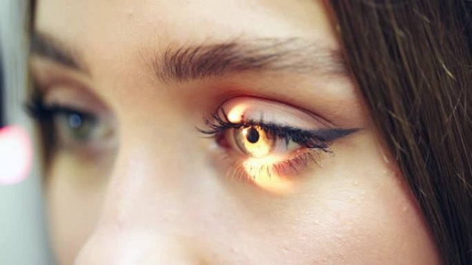 年轻女性向医生检查眼睛。明亮的光线照在女人的眼睛里。眼睛和角膜护理的概念。特写。