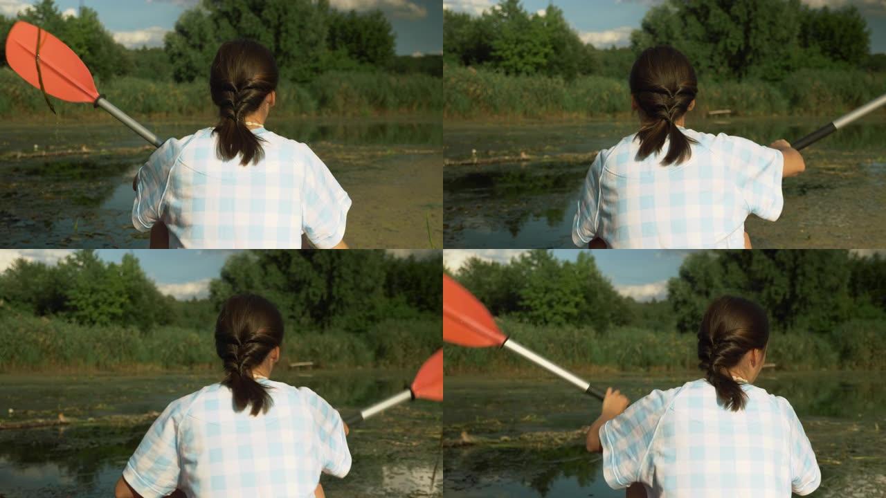 夏季，健身运动的女人漂浮在平静的河上的独木舟上，向后射击。女孩在暑假划皮划艇和探索河流。湖上船桨的年