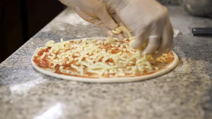 库克将磨碎的奶酪胡椒粉放在带有番茄酱的比萨饼上