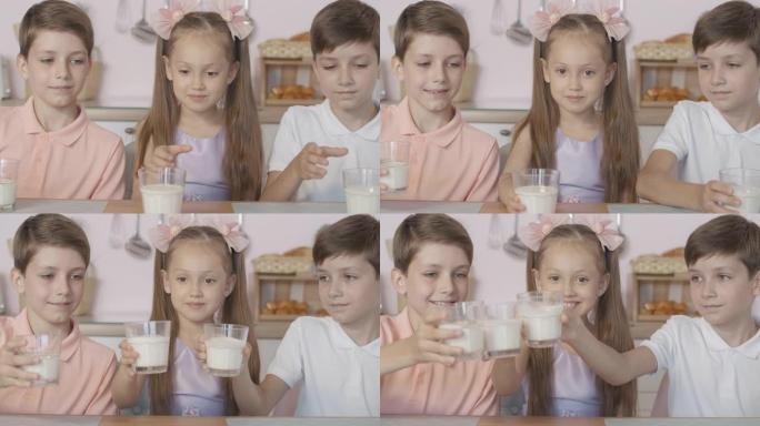 快乐的孩子用牛奶和微笑碰杯的特写镜头。欢快的小高加索双胞胎男孩和女孩的肖像在早上用乳品饮料吃早餐