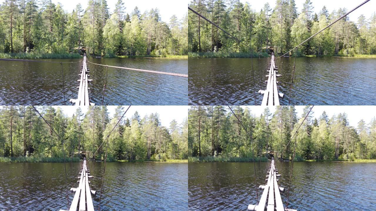 横跨湖的悬吊木桥。夏日。绿色森林。视图向下移动