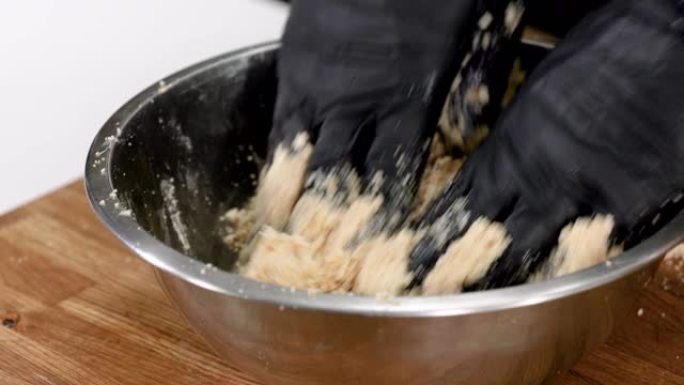 男人戴着黑色手套的手在碗里搅拌磨碎的饼干和黄油。4K