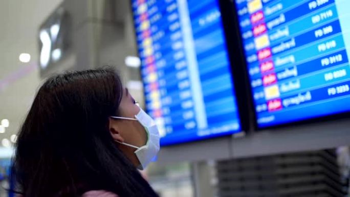 东南亚女性乘客戴着防护口罩查看航空公司时间表，在机场航站楼，新型冠状病毒肺炎大流行，旅行保险，公共交