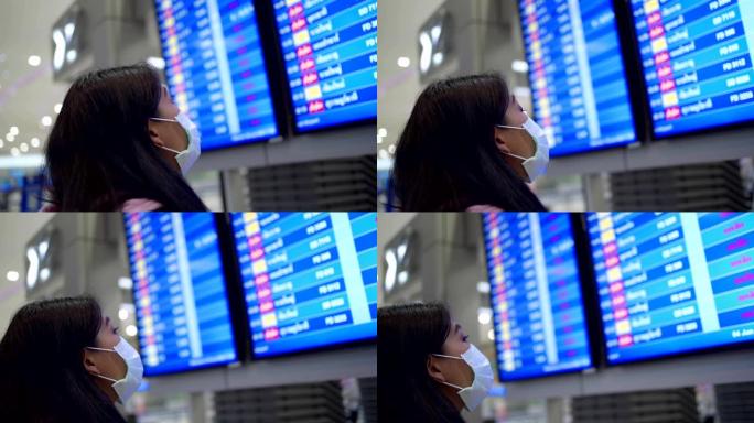 东南亚女性乘客戴着防护口罩查看航空公司时间表，在机场航站楼，新型冠状病毒肺炎大流行，旅行保险，公共交