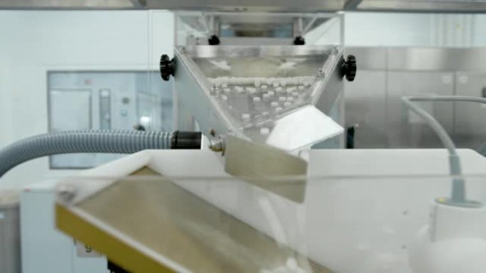 白色药丸在制药厂车间的金属自动线上移动。制药化学公司工作过程中药物沿传送带移动的特写视图