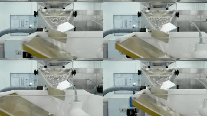 白色药丸在制药厂车间的金属自动线上移动。制药化学公司工作过程中药物沿传送带移动的特写视图