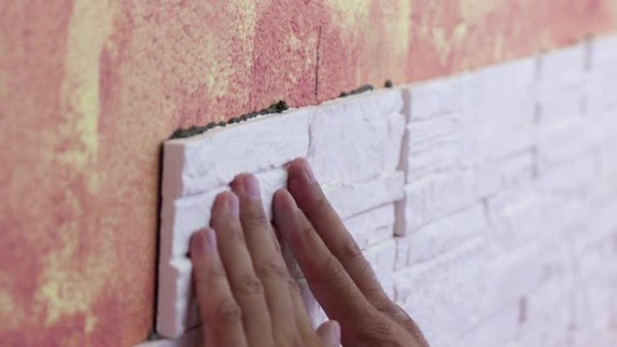 将瓷砖贴在墙上的手的特写。