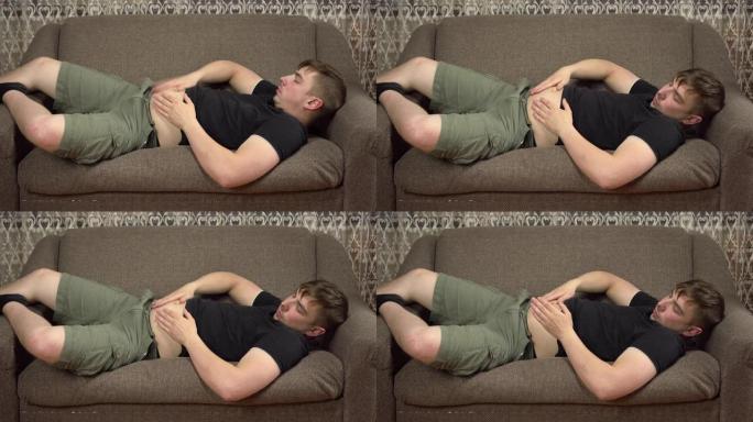 一个年轻人躺在沙发上拍着肚子。在检疫中增加了多余的体重。
