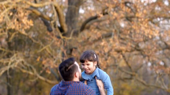 父亲带着女儿走在美丽的秋天森林里。穿着格子衬衫的胡子高个子男人扔着小女孩，围着她玩。父亲节概念。50