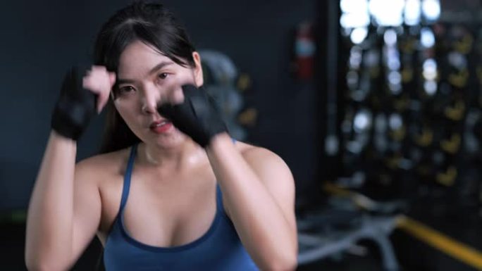 特写动作镜头: 运动的年轻亚洲女性拳击手戴着腕带，穿着运动服的女性准备拳击练习或锻炼。运动员适合健身