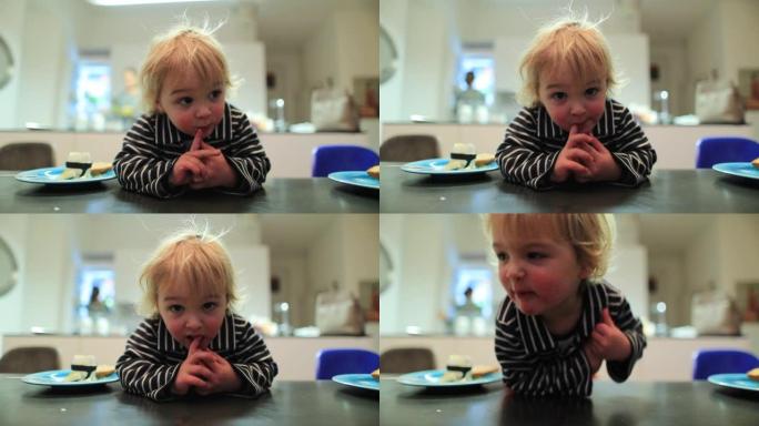 厨房桌子上的男婴肖像由相机快乐，背景中坦率的妈妈主演