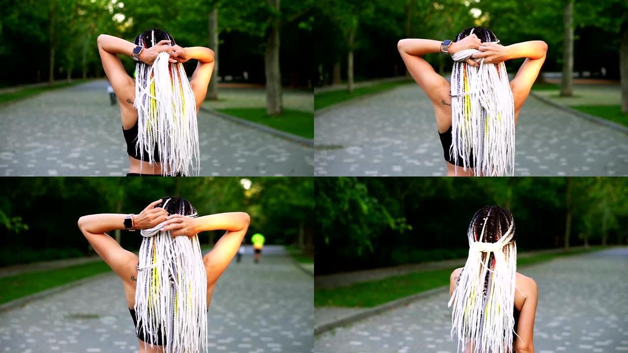 一个女孩背上的黑白辫子。一个运动女孩打结头发并开始在绿色公园跑步的后视图