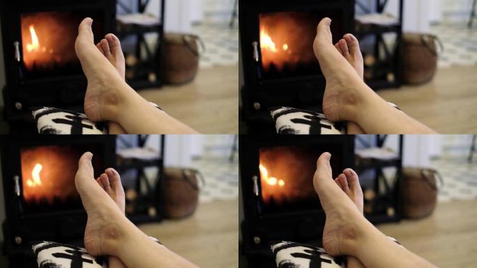 女性腿在家庭壁炉和房子里的木柴的背景上。放松概念。
