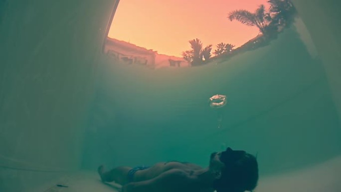 水下环形气泡。年轻的健美男子躺在游泳池的水下，将环形气泡吹到水面