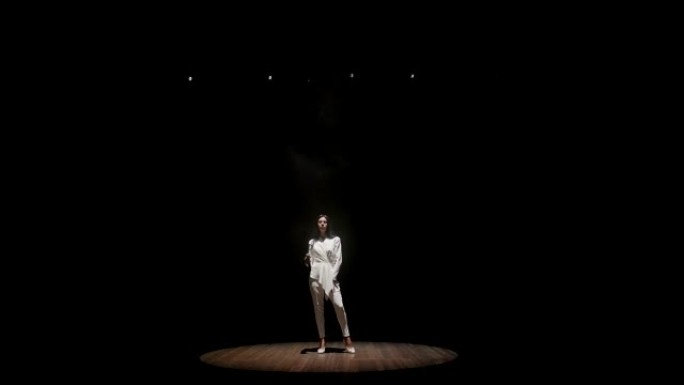 一位美丽的歌手在白色聚光灯下的黑暗中登台。