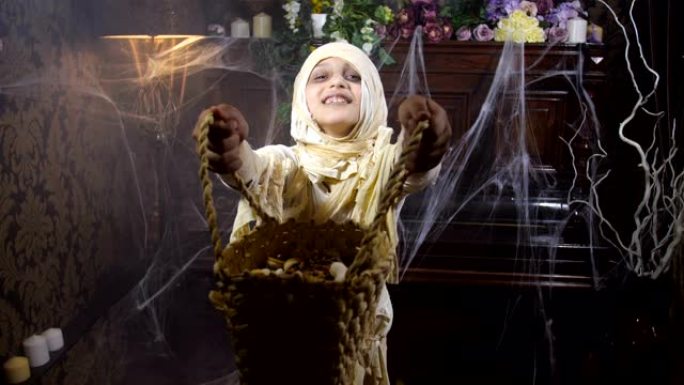 女孩穿着万圣节木乃伊服装，篮子在古老的黑暗哥特式室内跳舞，上面布满了蜘蛛网和神秘的雾，要求在那里享受