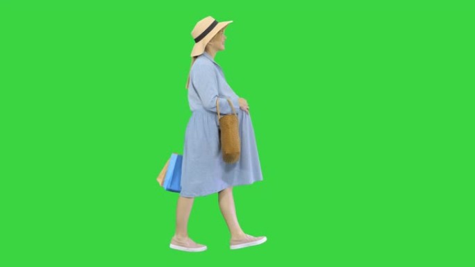 穿着夏装的孕妇带着购物袋走在绿屏上，色键