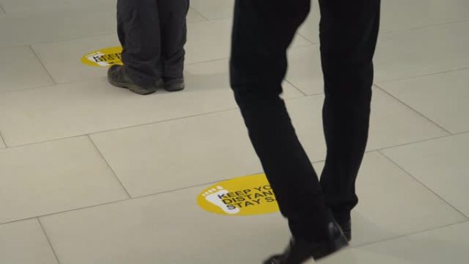 人们走在瓷砖地板上的社交距离标志上