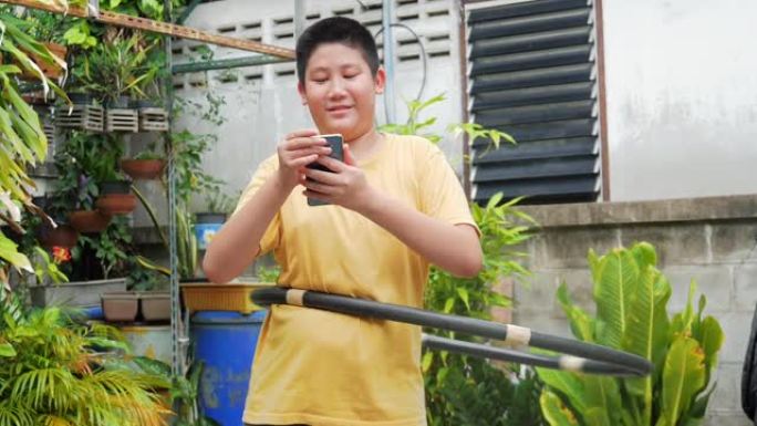 亚洲青春期男孩玩呼啦圈，在家后院使用智能手机，生活方式概念。