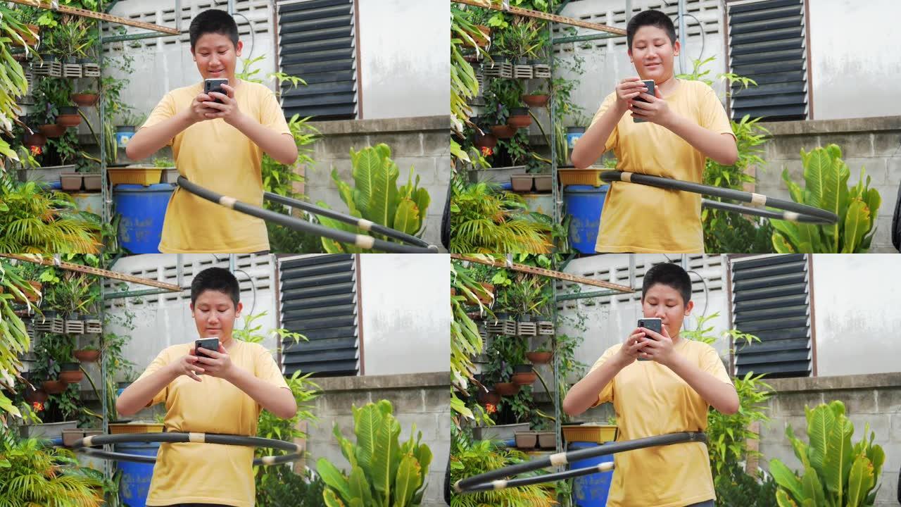 亚洲青春期男孩玩呼啦圈，在家后院使用智能手机，生活方式概念。
