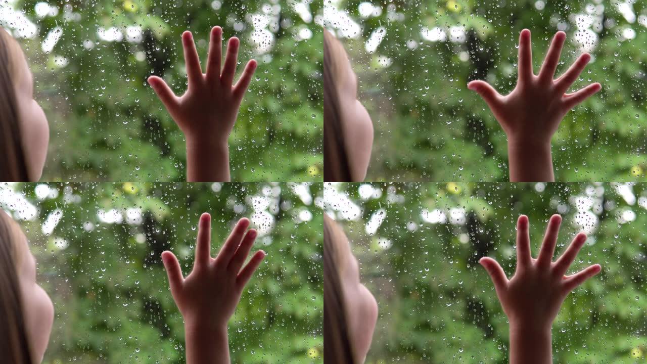 小女孩看着窗外的雨水和绿树。手放在玻璃上。