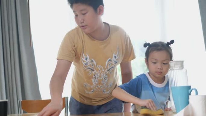亚洲兄弟在家吃完早餐后教妹妹清理餐桌，生活方式理念。