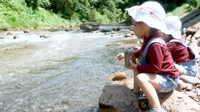 夏天，两个坐在河边一块岩石上的女孩在吃鱼时玩得很开心。家庭度假旅行。