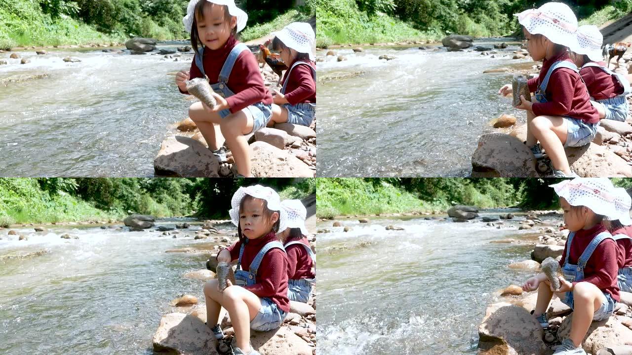 夏天，两个坐在河边一块岩石上的女孩在吃鱼时玩得很开心。家庭度假旅行。