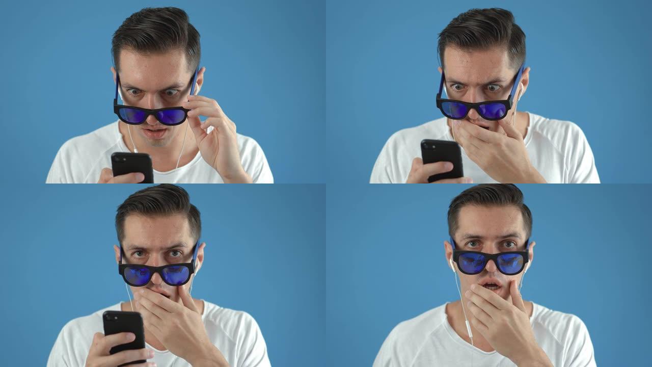 戴着太阳镜的震惊男子在智能手机上做出反应。令人不快的惊讶和害怕。男性对他在智能手机上看到的蓝色背景感