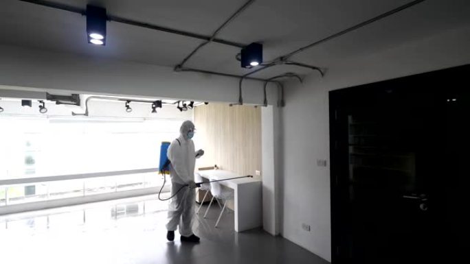 个人防护设备 (ppe) 工人在建筑物中使用喷雾消毒水清洁以去除covid 19