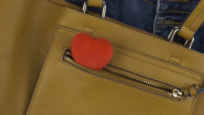 心脏从女性黄色袋子的口袋里伸出来。轮动。爱情和时尚的背景。