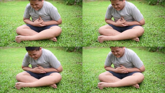 肥胖的胖男孩坐在草坪上因食物中毒而胃痛
