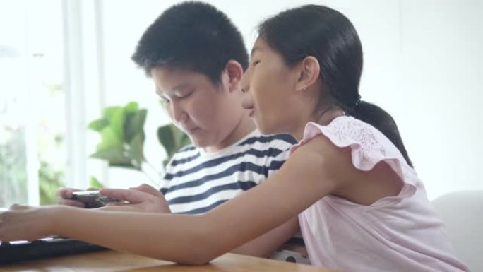 快乐的亚洲兄弟和她的妹妹玩游戏与笔记本电脑和智能手机在线竞争在家里，生活方式的概念。