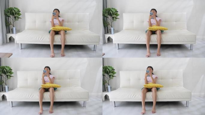 亚洲女孩使用智能手机在家里坐在沙发上看电影或玩游戏，生活方式概念。