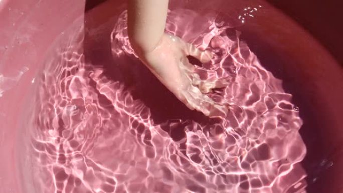 孩子在粉红色的水池里用清水洗手。夏季水上游戏